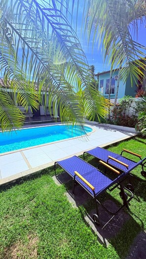 A swimming pool with lounge chairs, surrounded by palm trees and a building. - Terra do Sol Pousada (Porto Seguro)