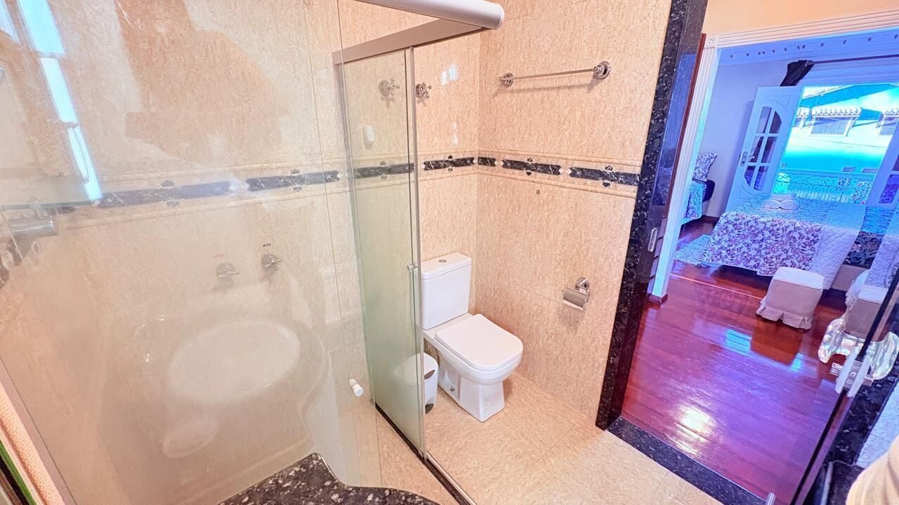 A bathroom with a glass-enclosed shower, a toilet, and a marble floor.
