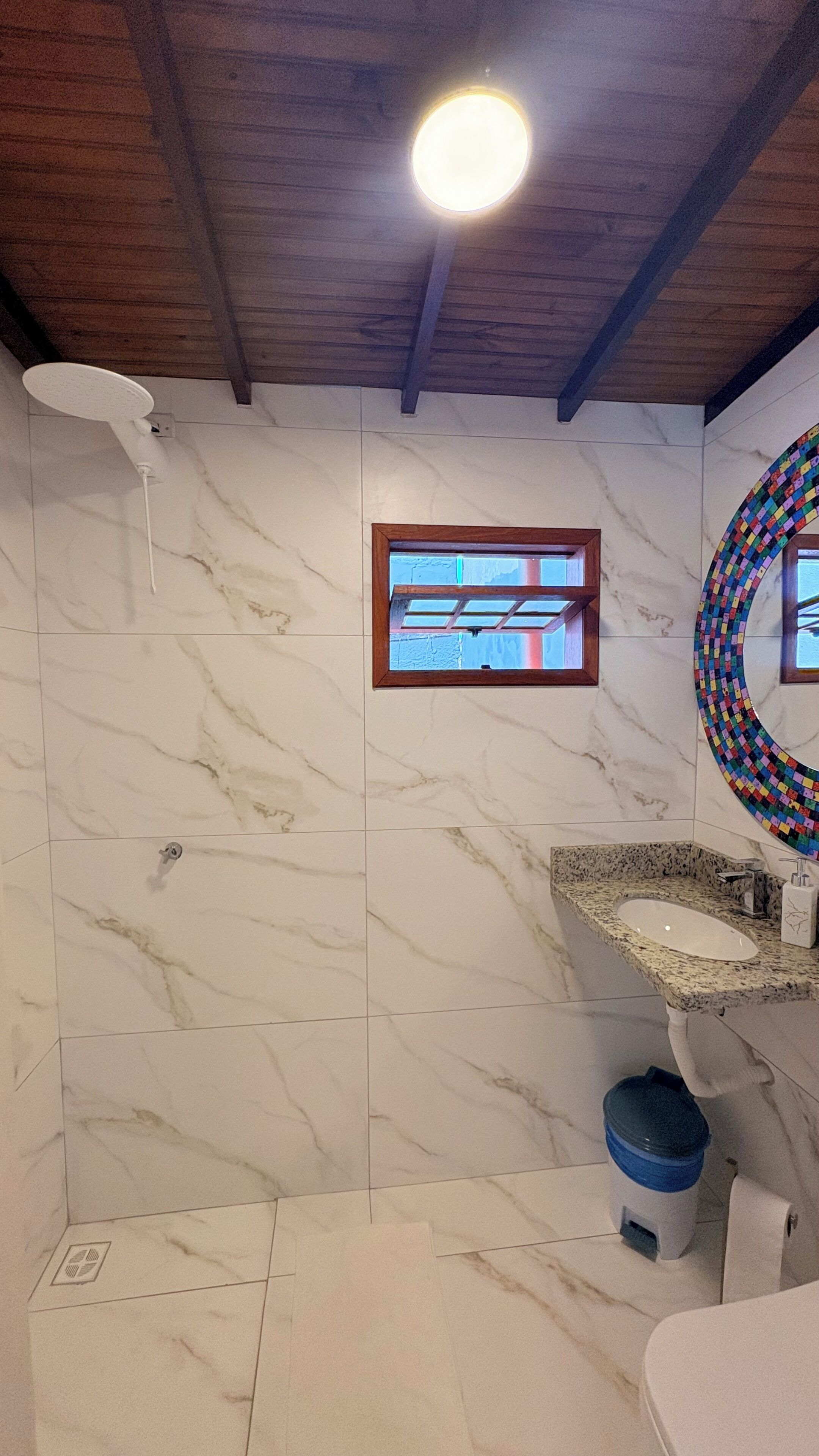 A bathroom with a marble wall, a wooden ceiling, a window, a sink, and a toilet.
