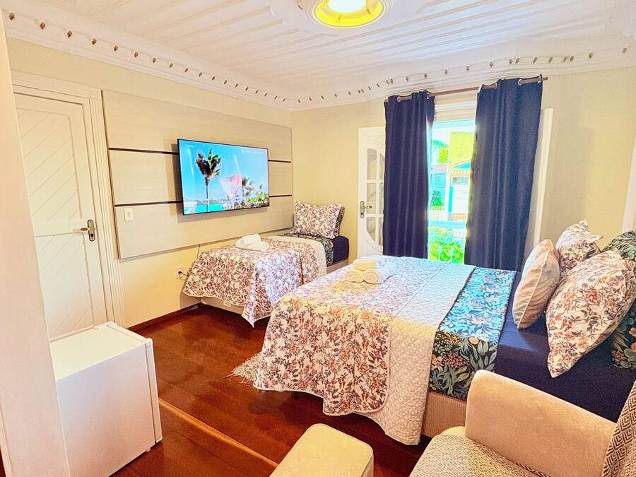 A room with two beds, a television, a window with curtains, and a door.
