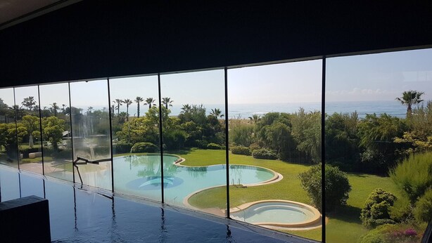 A large indoor swimming pool with a view of a landscaped garden and the ocean. - Gava Mar Apartment With Beach View (Gava)