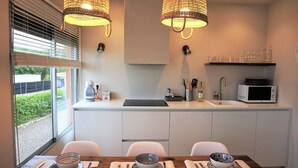 A modern kitchen with a dining area, featuring a large window, two pendant lights, a microwave, and a sink. - Gava Mar Apartment With Beach View (Gava)