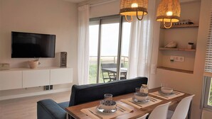 A modern dining area with a wooden table, white chairs, and a television mounted on the wall. - Gava Mar Apartment With Beach View (Gava)
