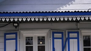 Un banco blanco frente a un edificio con contraventanas azules y una puerta blanca.