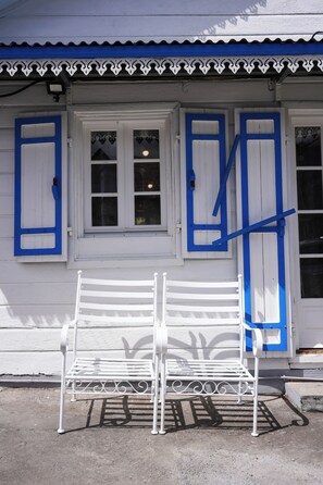 Un banc blanc se trouve devant un bâtiment aux volets bleus et à la porte blanche.