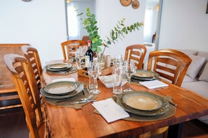 Une table de salle à manger en bois, mise avec des assiettes, des verres et une bouteille de vin, entourée de chaises en bois.