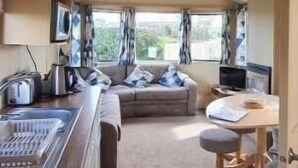 A compact RV interior with a kitchenette, a seating area, and a window providing a view of the outdoors.