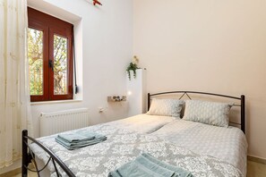 A bedroom with a bed, a window with curtains, a radiator, a wall-mounted plant, and a bedside table with a lamp.