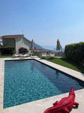 Una piscina con agua cristalina, una escultura de cocodrilo rojo y vistas al mar y a las montañas.