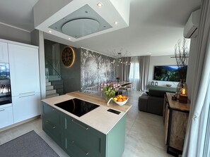Una cocina moderna con una isla central, un comedor con vistas y un espacio de sala con televisor y objetos decorativos.