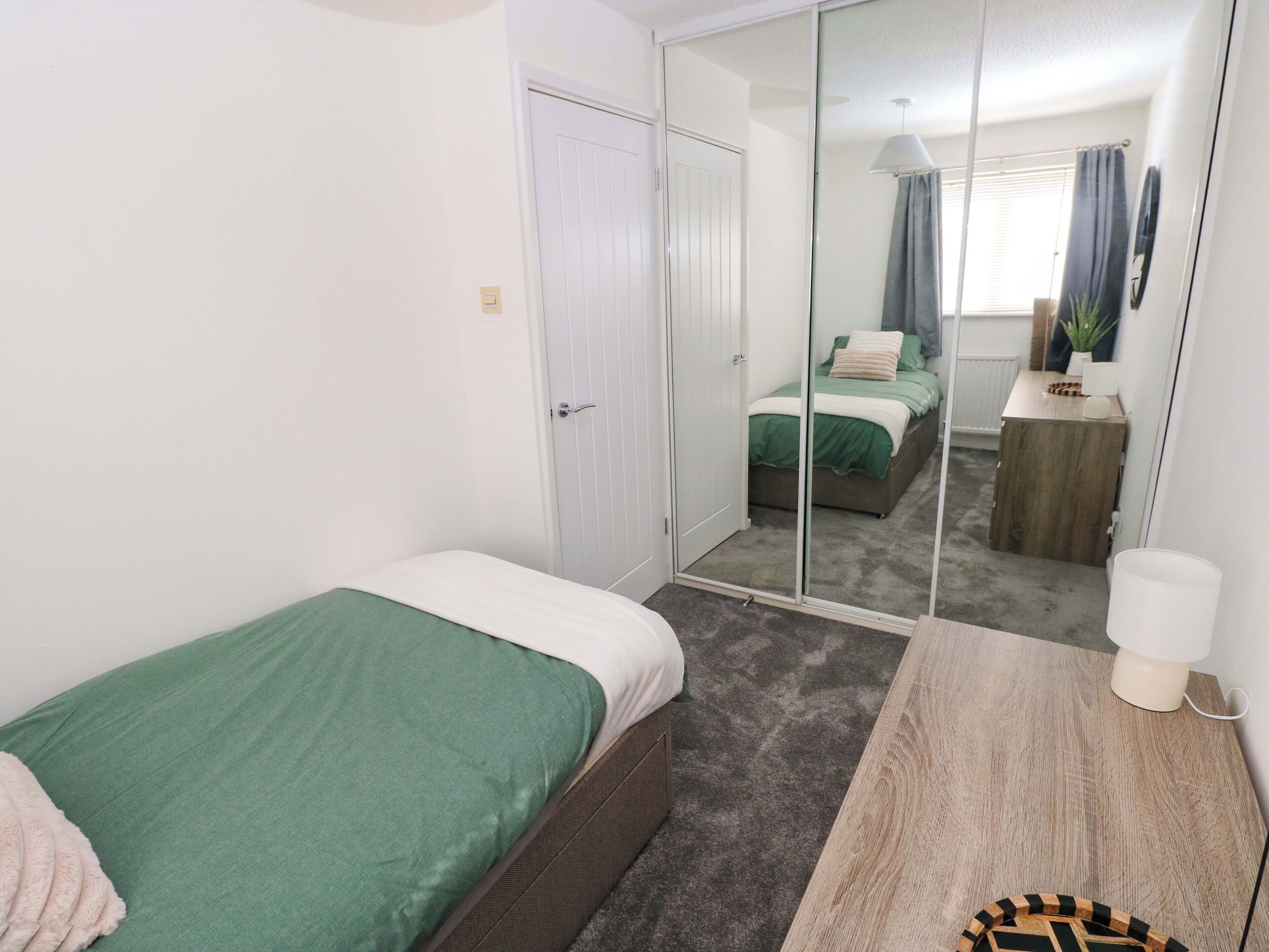 Quarto com uma cama de solteiro, espelho, mesa de cabeceira e guarda-roupa.