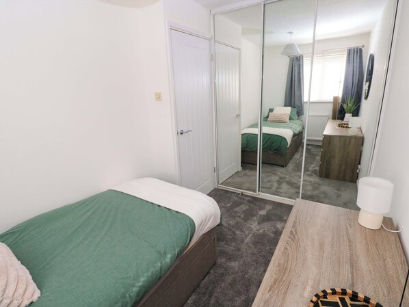 A bedroom with a single bed, a mirror, a bedside table, and a wardrobe. - The Gower Gateway (Swansea)