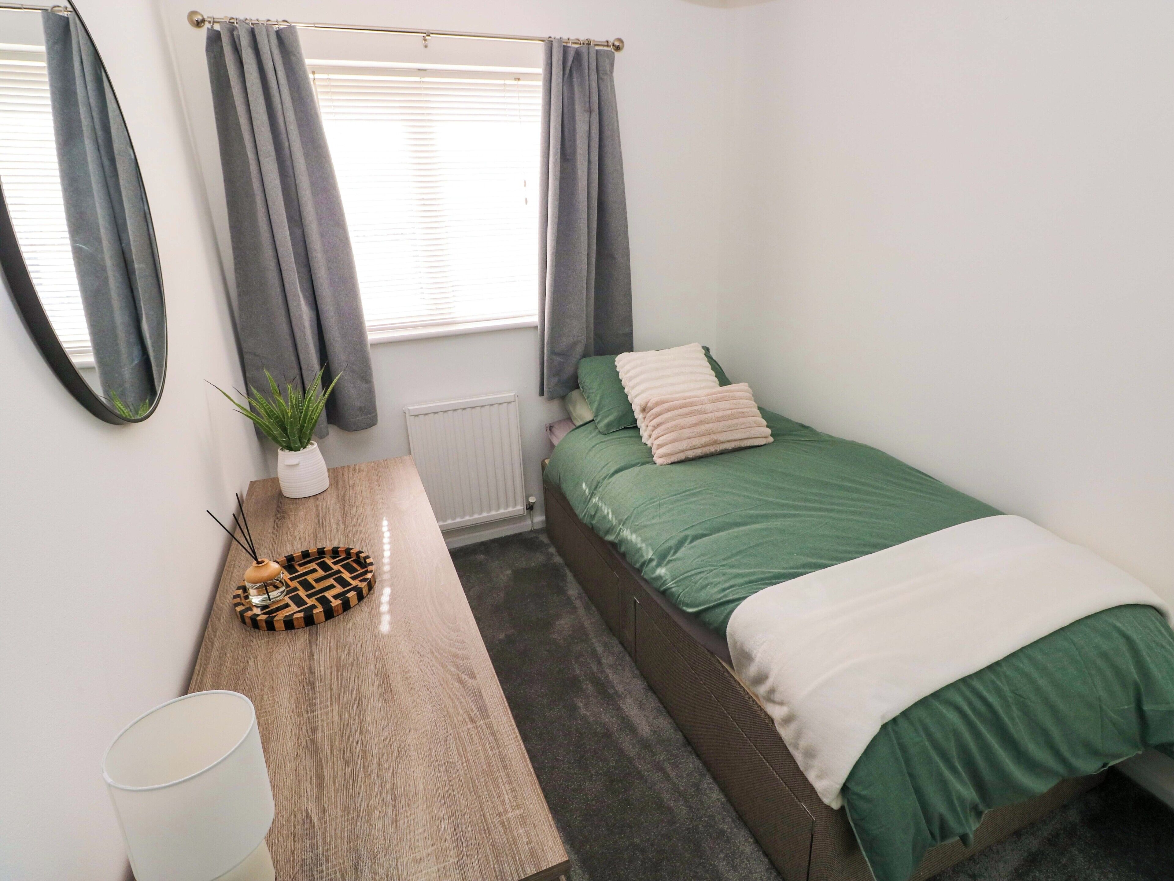 Quarto com cama, mesa de cabeceira com abajur, espelho, planta em vaso e radiador.