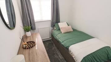 Quarto com cama, mesa de cabeceira com abajur, espelho, planta em vaso e radiador.
