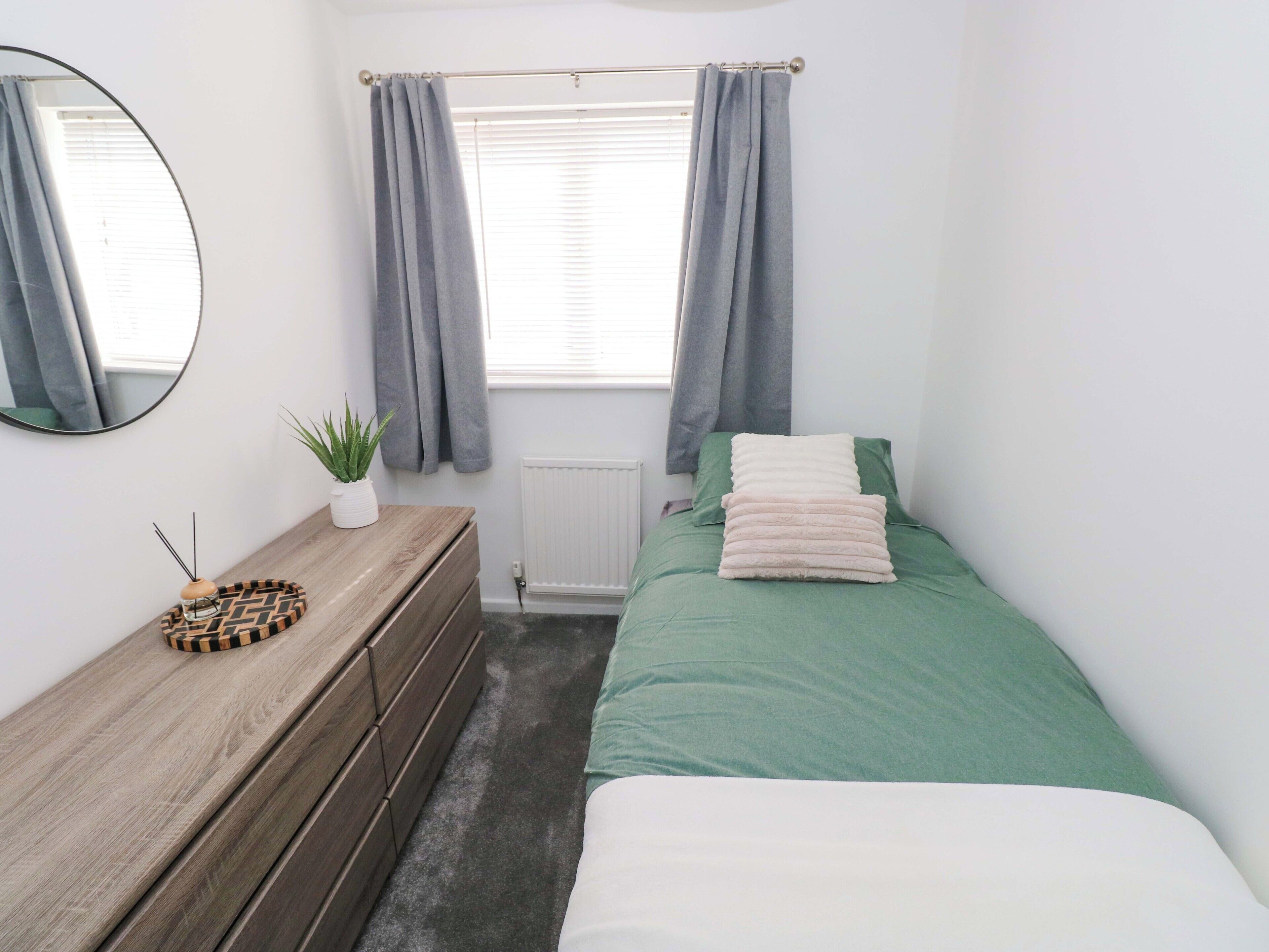A bedroom with a bed, a dresser, a mirror, a window with curtains, and a radiator.