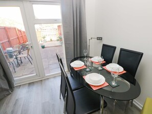 A dining area with a glass table, black chairs, and a view of a backyard through a sliding door. - The Gower Gateway (Swansea)