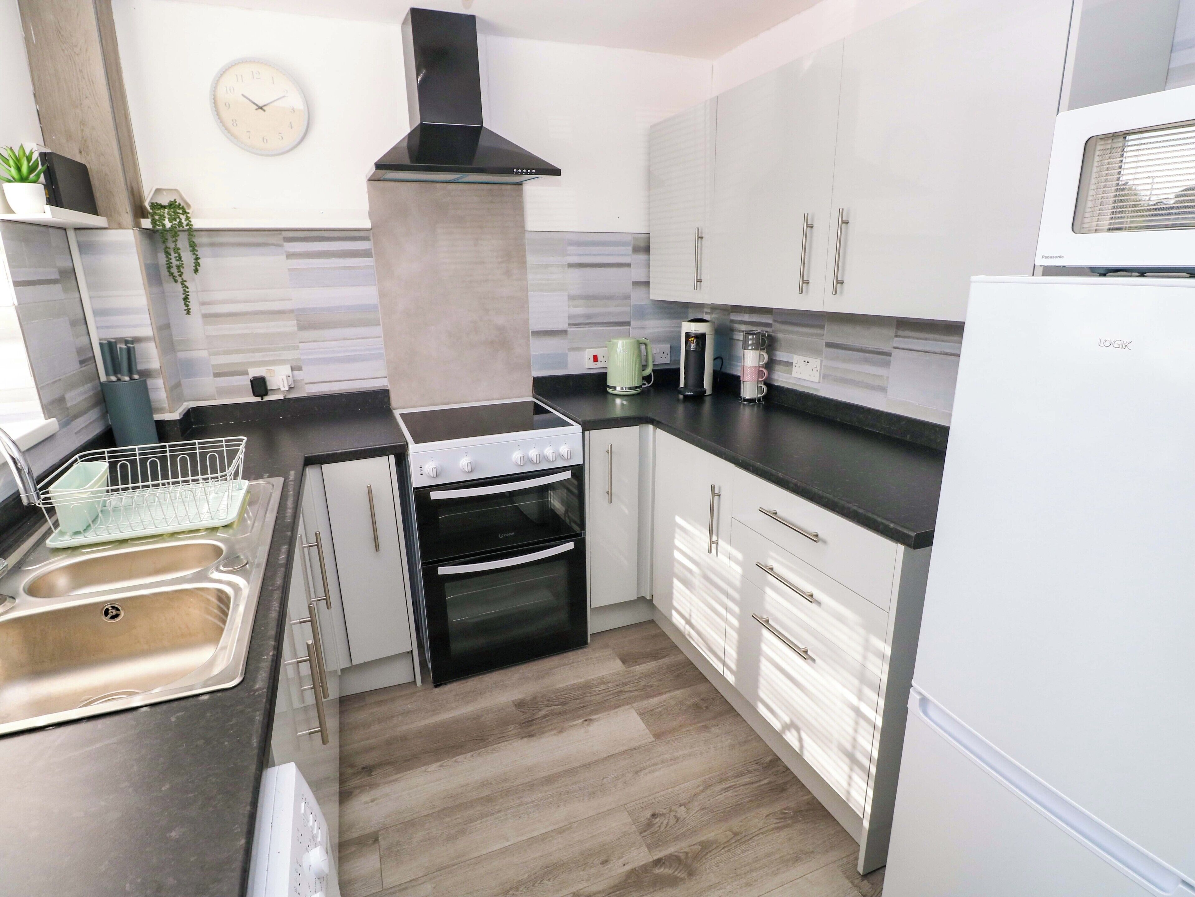 Cozinha moderna com fogão a gás, forno, armários brancos, exaustor preto, micro-ondas e lava-louças.