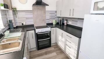 Cozinha moderna com fogão a gás, forno, armários brancos, exaustor preto, micro-ondas e lava-louças.