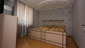 A bedroom with a bed, curtains, a television, and a ceiling light fixture.