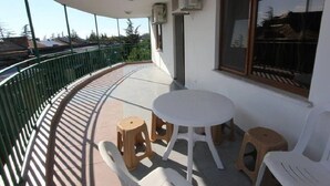 A balcony with a round table and four stools, air conditioning units, and a view of the surrounding area.