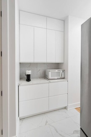 Une cuisine avec des meubles blancs, un four à micro-ondes et une machine à café.