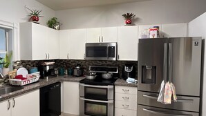Een moderne keuken met witte kastjes, een roestvrijstalen koelkast, een magnetron en een fornuis.