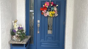 Een blauwe deur met een bloemenkrans, een deurmat en een kleine tafel met een beeldje.