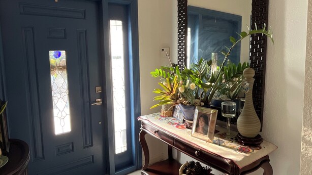 Een blauwe deur met een glas-in-loodraam, een console tafel met planten en een vaas, en een grote spiegel aan de muur.