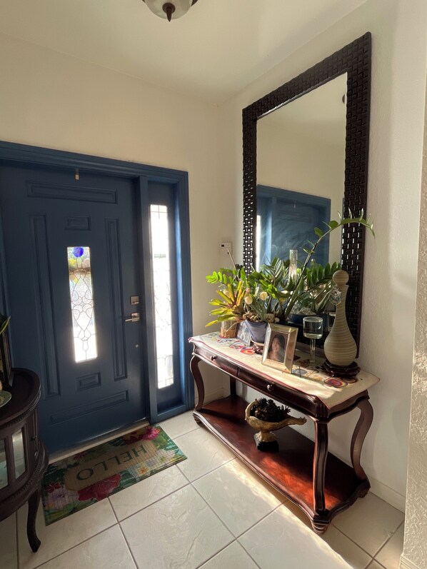 Une porte bleue ornée d’un vitrail, une console sur laquelle sont disposées des plantes et un vase, et un grand miroir accroché au mur.