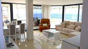 Ein modernes Wohnzimmer mit einer Couch, Sesseln, einem Couchtisch und einem Essbereich mit Stühlen und einem Tisch.