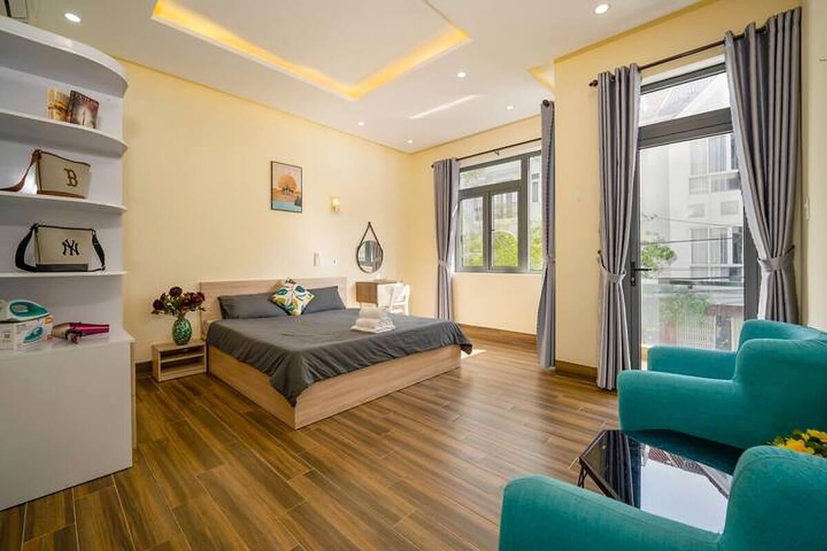 A modern hotel room with a bed, a seating area, a shelf with bags, and a window with curtains.