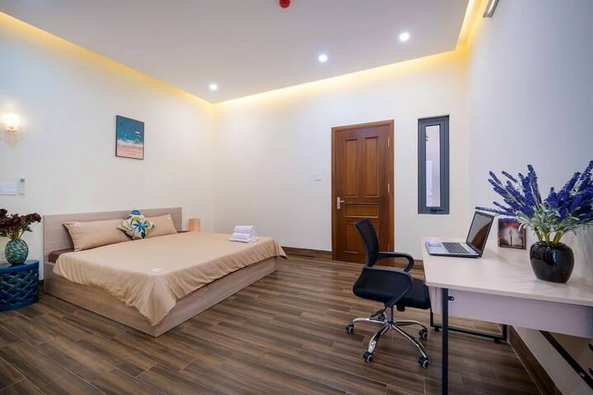 A hotel room with a bed, desk, chair, and a door.