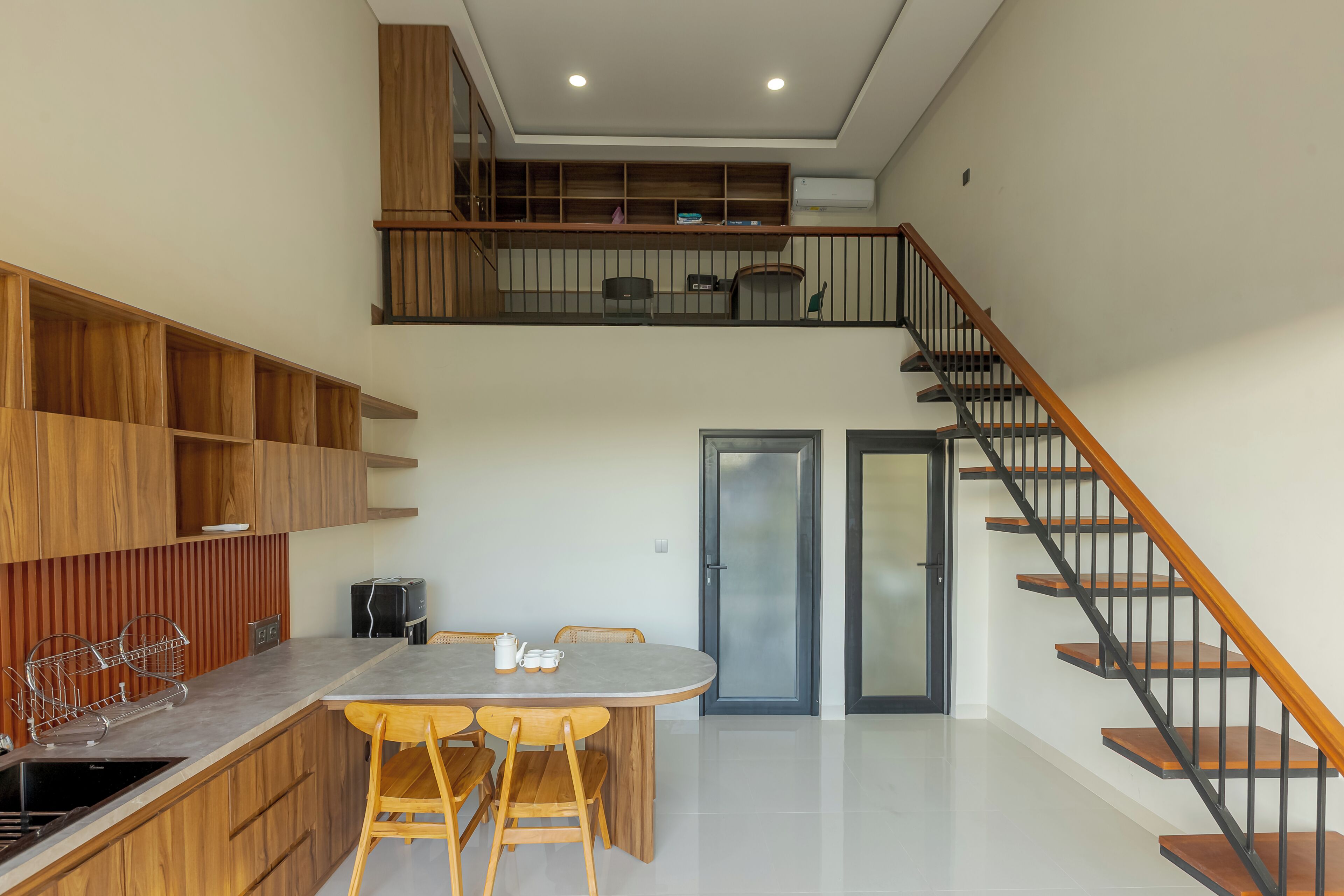 A modern kitchen with wooden cabinets, a dining table with chairs, a staircase, and a small balcony.