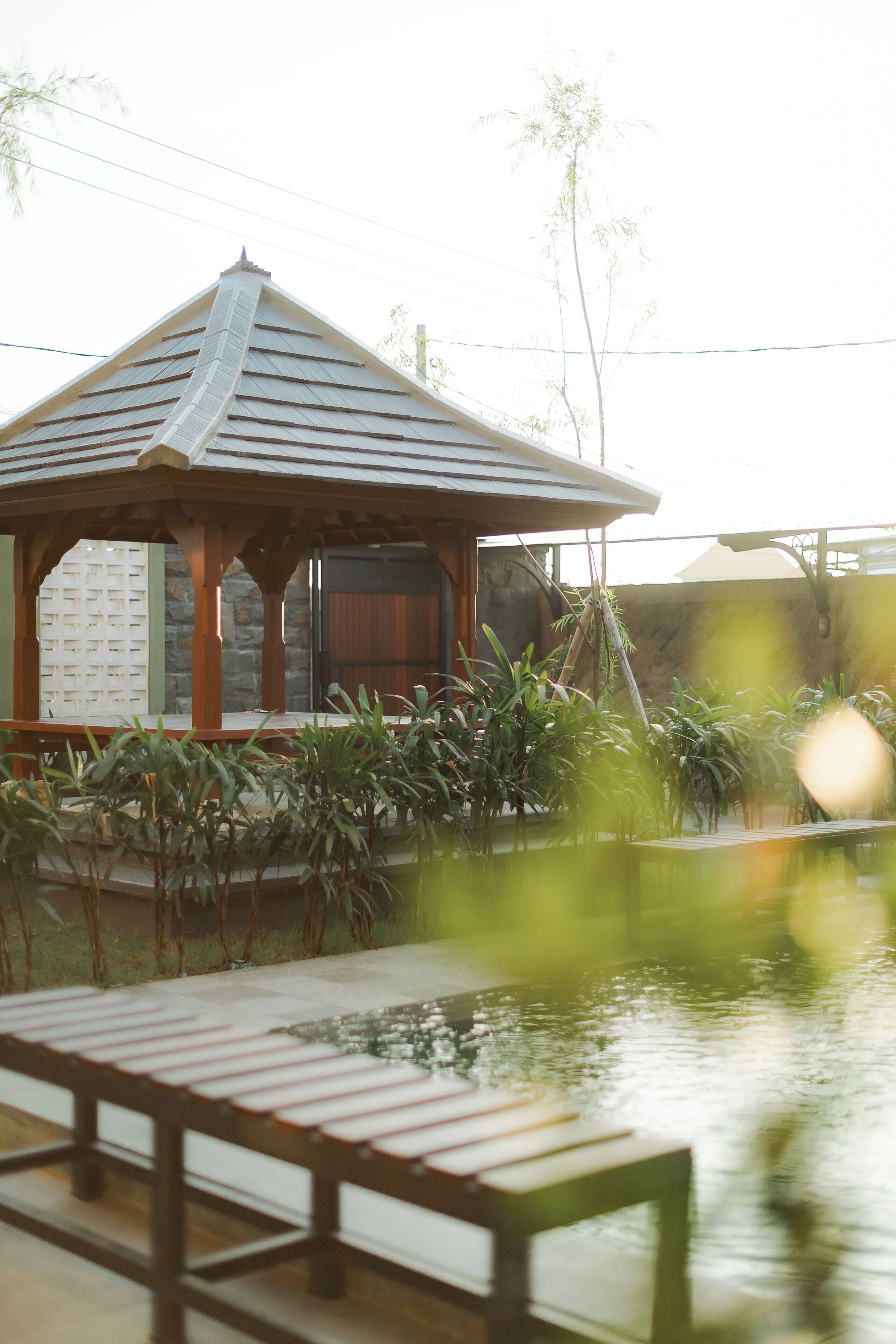 A gazebo with a tiled roof, surrounded by greenery and a small pond.