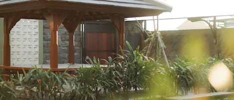 A gazebo with a tiled roof, surrounded by greenery and a small pond.