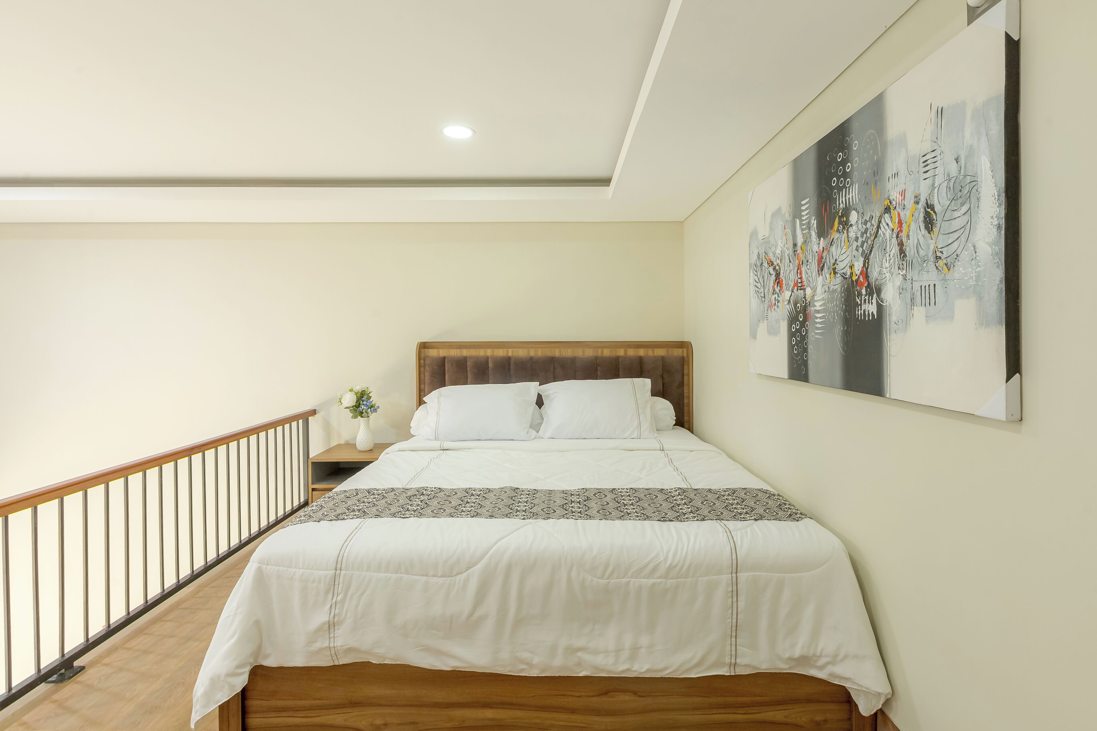 A bedroom with a bed, a nightstand, a wall-mounted painting, and a wooden railing.