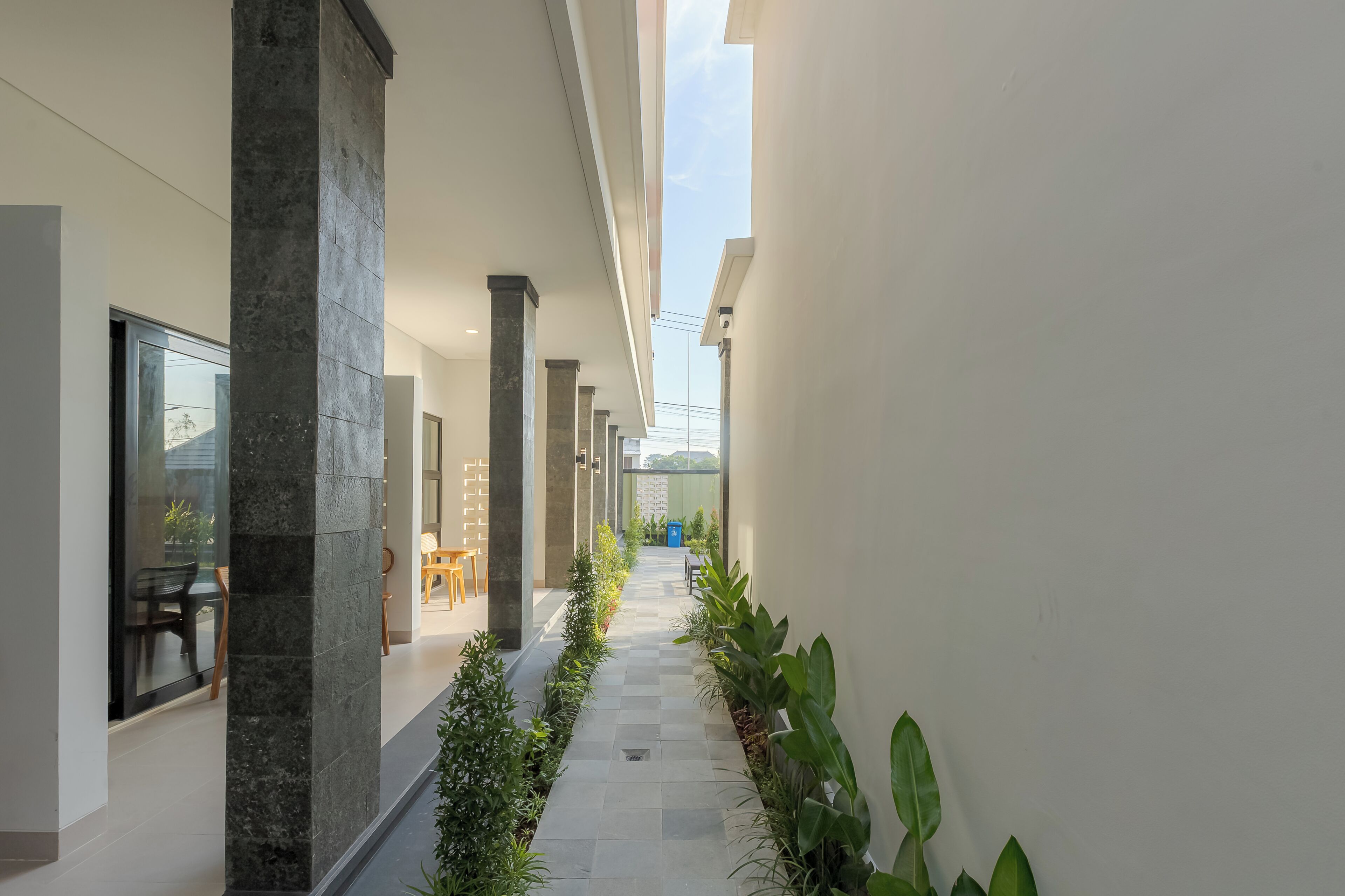 A corridor with a tiled floor, columns, and potted plants.