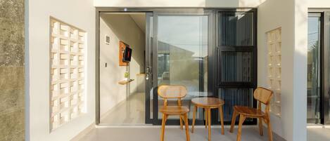 A modern interior with a glass door leading to a balcony, wooden chairs, and a small table.