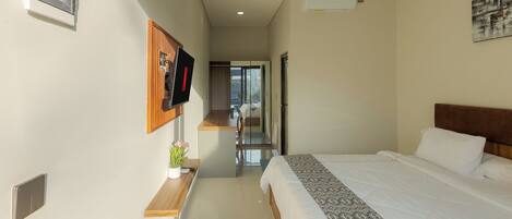 A modern hotel room with a bed, a TV mounted on the wall, a small wooden table with a plant, and a view through a glass door to the outside.