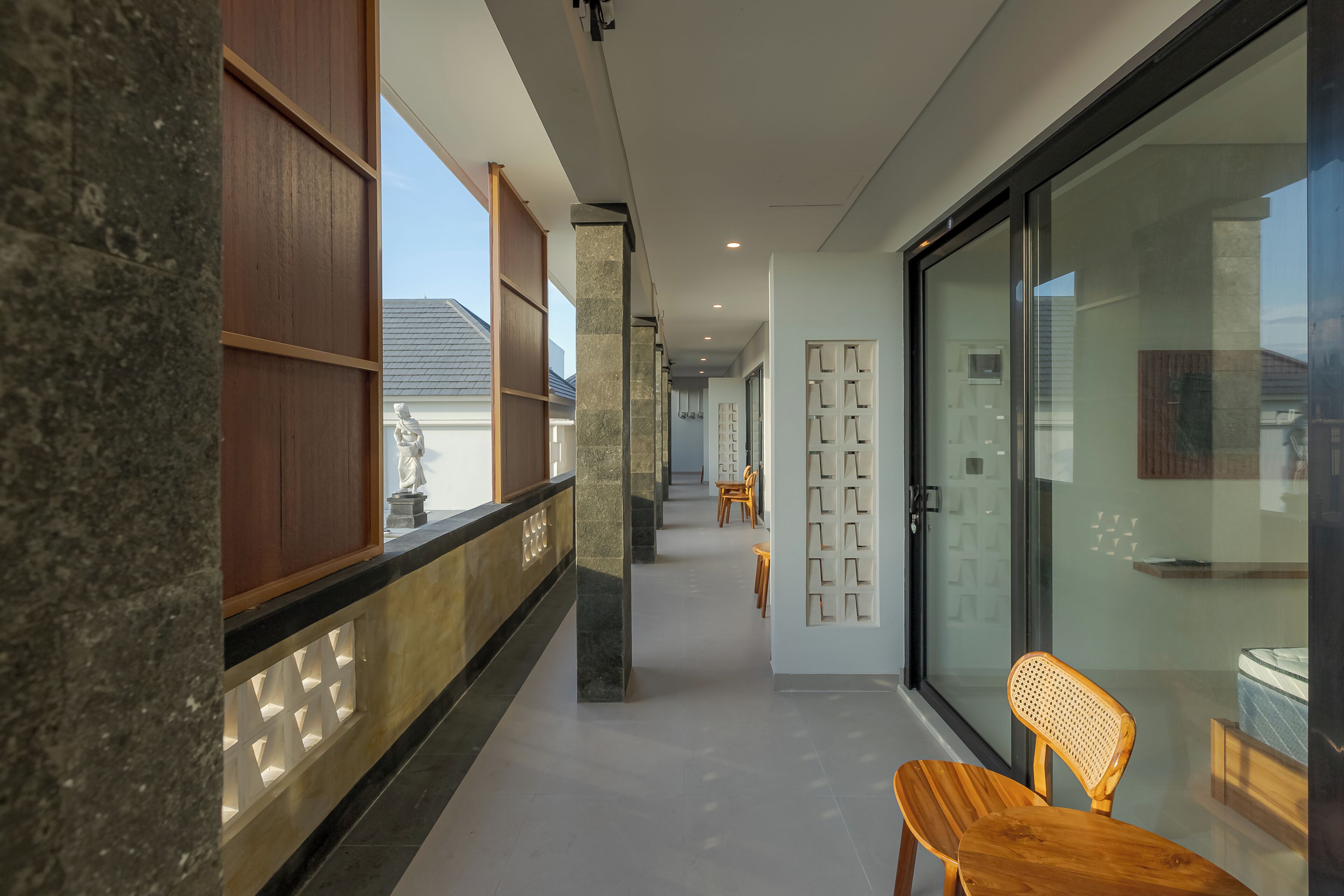 Un interior moderno con un pasillo que conduce a una habitación con puerta de vidrio, mobiliario de madera y una estatua.