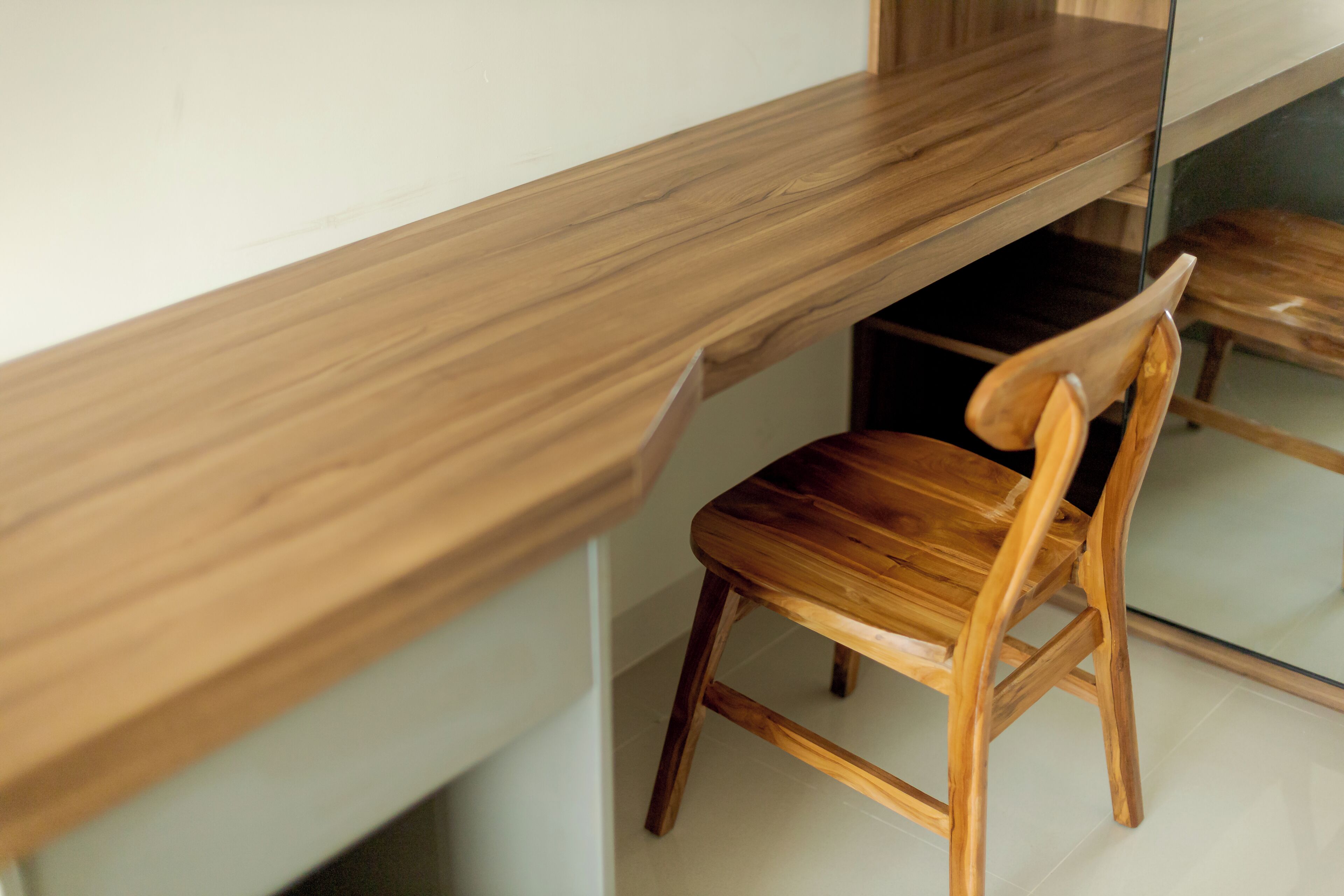 A wooden desk with a chair, a mirror, and a white wall.