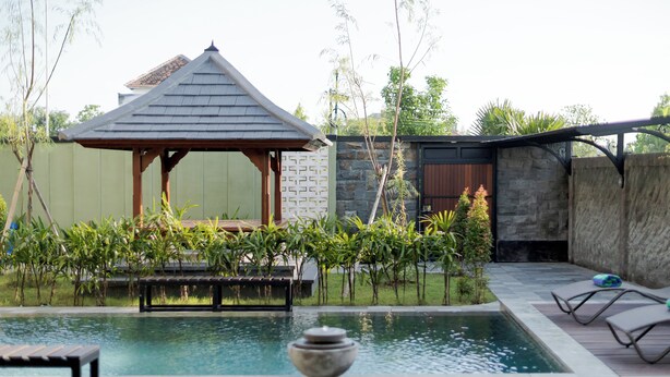 A pool area with a gazebo, lounge chairs, and a stone wall.