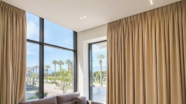 A modern living room with a sofa, large windows, and curtains. - Suites By Jordan's Hotel (Vlore)