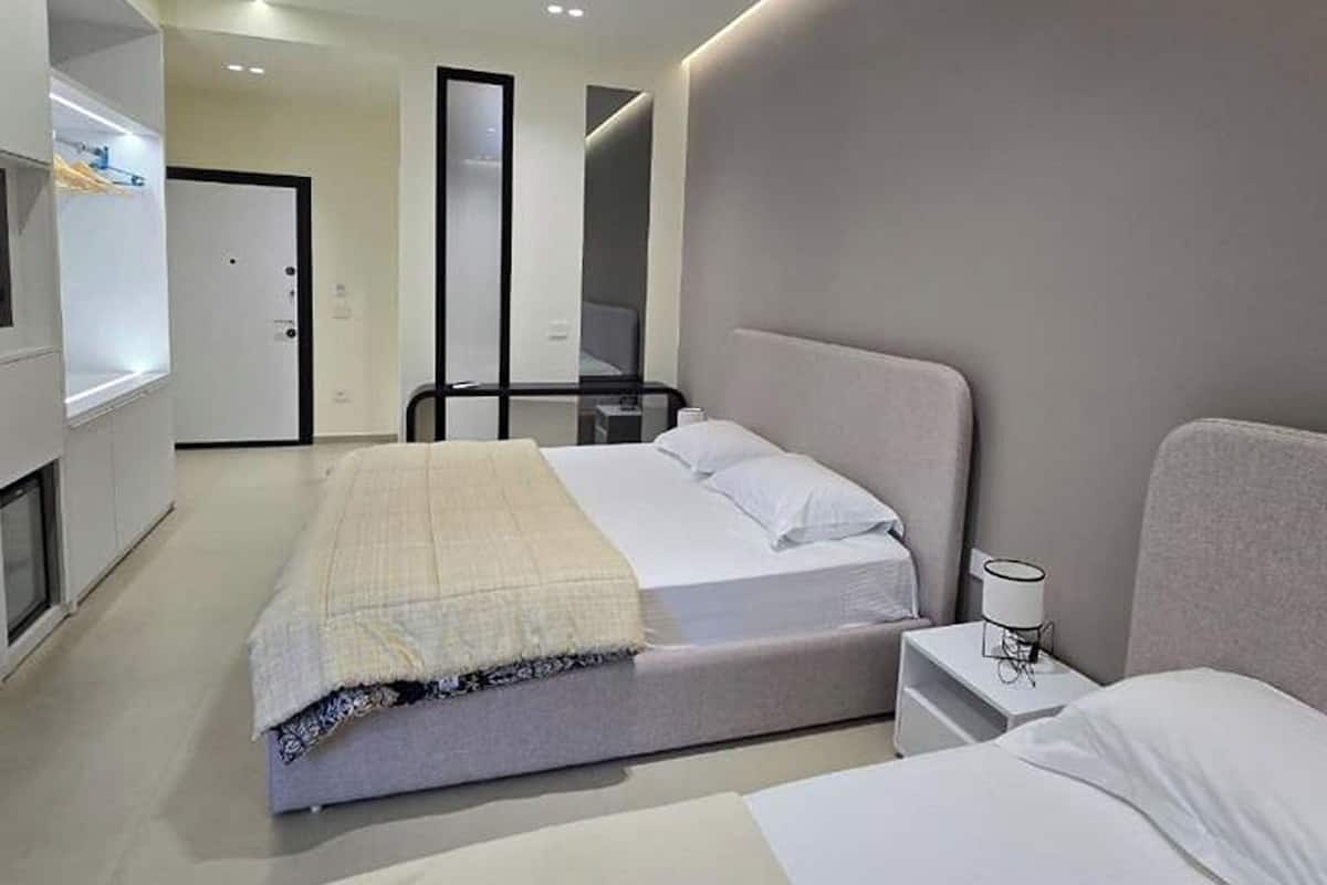A modern hotel room with a large bed, bedside tables, a wardrobe, and a mirror.