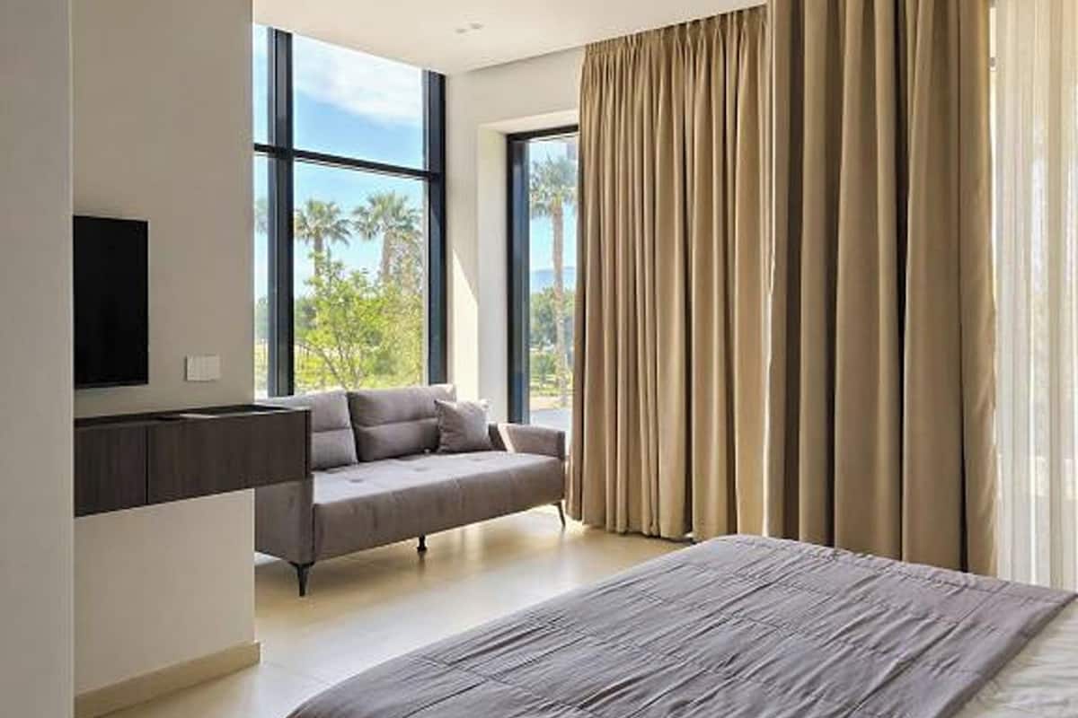 A modern bedroom with a large bed, a sofa, and a TV mounted on the wall.