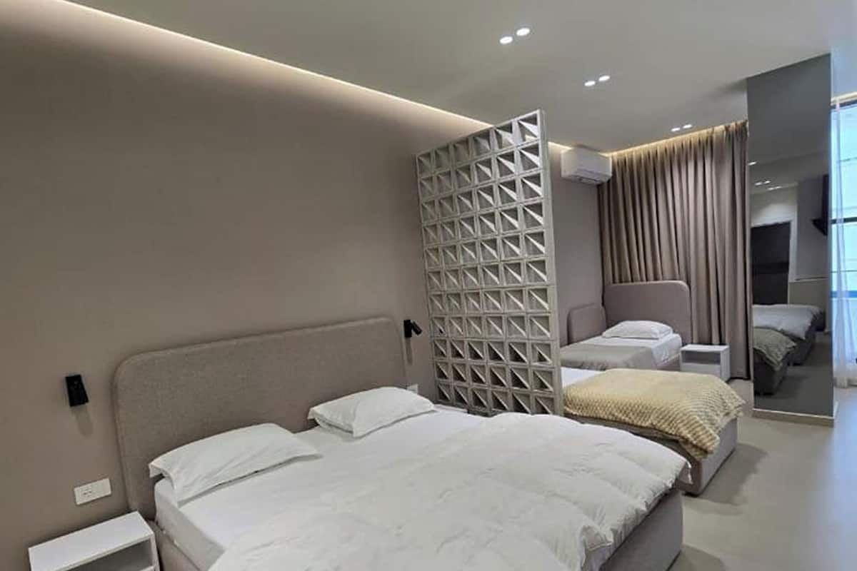 A modern hotel bedroom with a large bed, bedside tables, a seating area, and a partition wall.