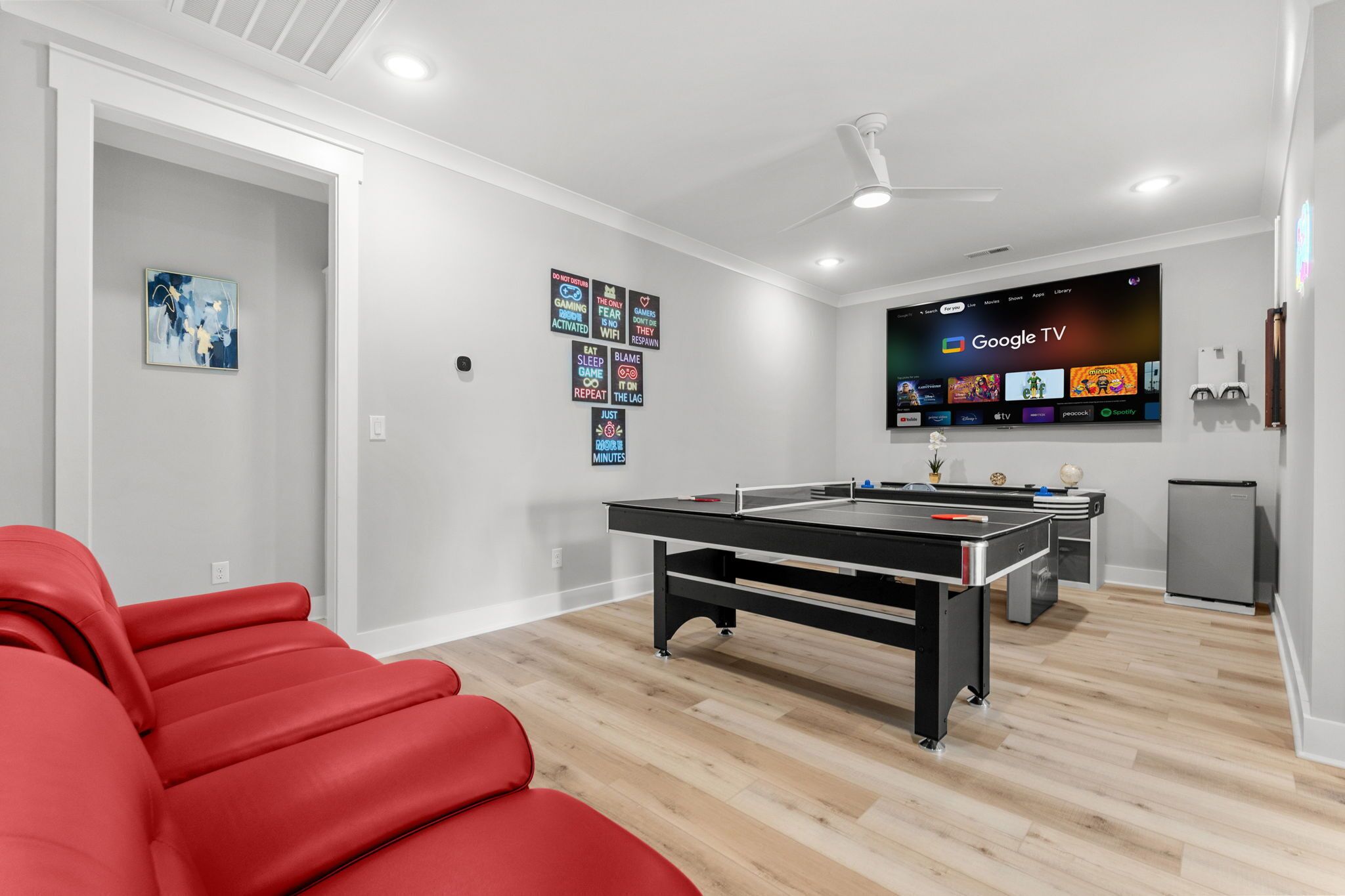 A modern living room with a pool table, red seating, a flat-screen TV displaying Google TV, and a ceiling fan.