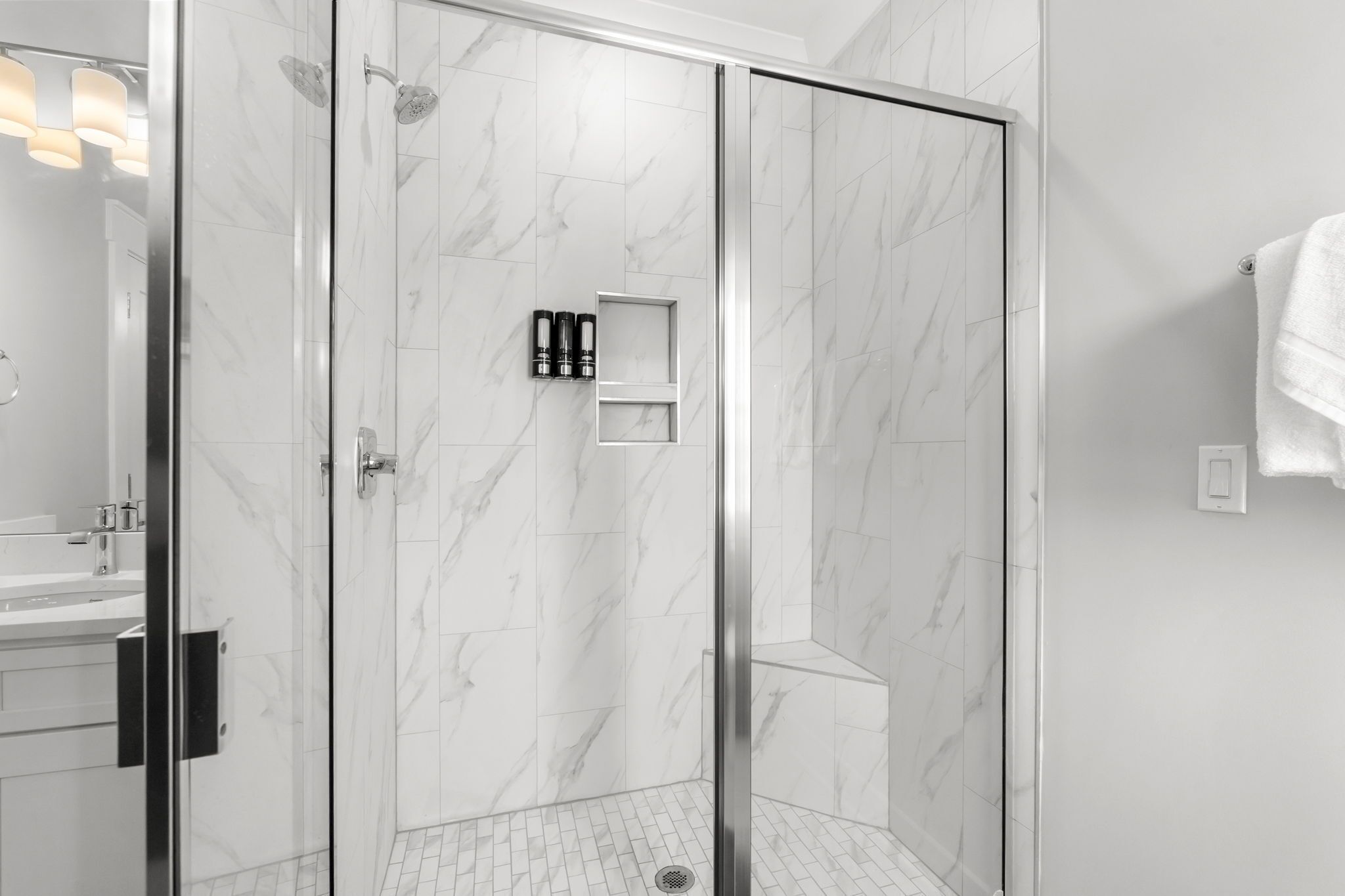 A modern bathroom with a glass-enclosed shower, marble tiles, a vanity with a mirror, and a towel rack.