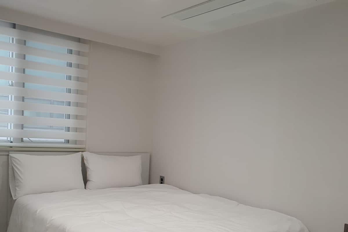 Una camera da letto con due letti, una finestra con tende, una plafoniera e una griglia di aerazione.