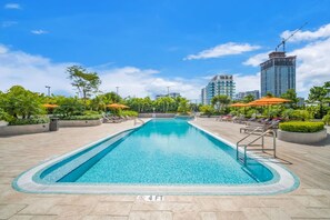 Ein rechteckiger Swimmingpool mit einer Tiefenmarkierung von 1,2 Metern, umgeben von Liegestühlen und Sonnenschirmen, mit Gebäuden im Hintergrund.
